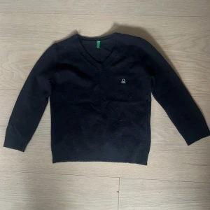 Svart v-ringad tröja från Benetton - Svart v-ringad tröja från Benetton med liten broderad logga på bröstet. Tröjan är långärmad och har ribbade muddar vid ärmslut och nederkant. Perfekt för lager-på-lager och enkel att matcha med olika outfits. ‼️Aldrig använd‼️ orginal