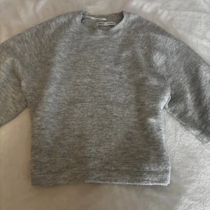 Grå stickad tröja från ONLY - Mysig grå stickad tröja från ONLY med rund halsringning och lång ärm. Enkel och stilren design som passar perfekt till jeans eller kjol. Tröjan har en mjuk känsla och är lätt att matcha med andra plagg.