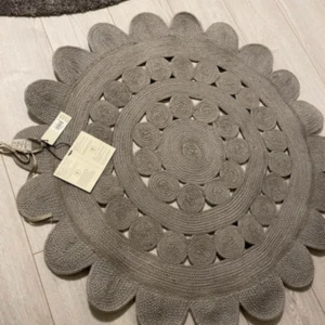 Elsaform Matta Blomma 120cm - Snygg rund matta från Elsaform i blomformad design, diameter 120 cm. Tillverkad av återvunnen PET, slitstark och lättskött. Mattan är oanvänd och har kvar originaletiketter. Perfekt för hall, sovrum eller vardagsrum. Inga synliga defekter eller slitage.