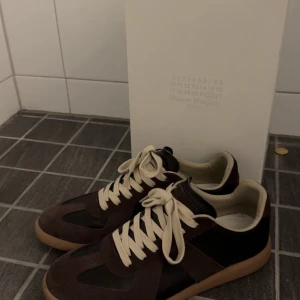 Maison Margiela sneakers brun/svart - Maison Margiela skor i storlek 43 dem är äkta men finns dock inget kvitto. Sjukt bra kvalite på dem, de är som nya säljs pga jag behöver pengar. Pris ej hugget i sten!