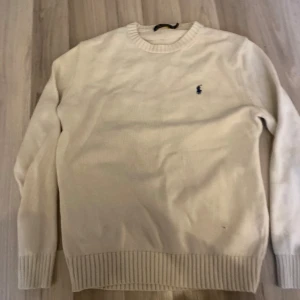 stickad tröja från Polo Ralph Lauren - Klassisk beige stickad tröja från Polo Ralph Lauren med rund halsringning och diskret broderad logga på bröstet. Tröjan har ribbade muddar vid ärmslut och nederkant, perfekt för en clean och stilren look. Skriv vid funderingar!