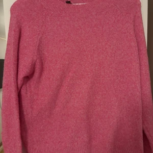 Rosa stickad tröja från Vero Moda - Mysig rosa stickad tröja från Vero Moda med rund hals och ribbade muddar vid hals, ärmslut och nederkant. Perfekt för att hålla värmen under kyliga dagar och har en enkel, klassisk design som är lätt att matcha med jeans eller kjol. Helt oanvänd