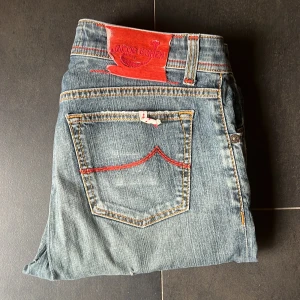 Jacob Cohen jeans - Säljer ett par Jacob Cohën jeans i modell 688, storlek W34 men små i storlek Fina detaljer med röd brodyr på fickorna och rött pälsemblem bak. Lite defekter på märket bak men inget som märks vid användning.  Kvalitetsjeans från italienska Jacob Cohën – kända för sin exklusiva denim och handgjorda känsla.  Längd 101 cm, bredd 42 cm.  Fraktar oftast samma dag!  ✅ Använda men i fint skick ✅ Mjuka och bekväma ✅ Äkta vara  Perfekta för dig som vill ha ett par jeans med premiumkänsla och snygga detalj