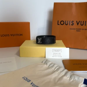 L och V svart läderarmband - Snyggt svart armband från L och V i äkta läder med silverfärgad L och V-logga. Armbandet har diskret monogrammönster och klassisk design som passar perfekt till din outfit. Kommer med originalpåse, ask och certifikat.