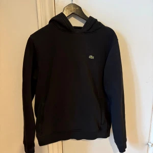 Lacoste hoodie junior  - Svart hoodie med två fickor med dragkedja. 