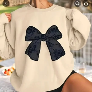 Beige sweatshirt med stor svart rosett - Trendig beige sweatshirt med oversized passform och lång ärm. Framtill finns en stor svart rosett med spetsdetaljer som ger en unik look. Perfekt för dig som vill sticka ut med en söt och cool vibe. Mjuk och skön, passar till jeans eller kjol.