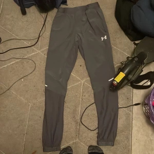 Grå träningstights från Under Armour XS - Grå träningsbyxor från Under Armour i storlek XS. De har en tight passform, elastisk midja och logga på låret. Tillverkade i ett stretchigt syntetmaterial som passar perfekt för träning och sportiga aktiviteter. Dom är i bra skick förutom de lilla brännmärket på benet