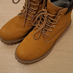 Bruna boots från New Yorker strl 43 - Säljer ett par snygga bruna boots från New Yorker i storlek 43. Skorna har grov sula med bra grepp, snörning med metallöglor och mjukt foder på insidan. Perfekta för höst och vinter, tillverkade i syntetmaterial med klassisk rund tå.