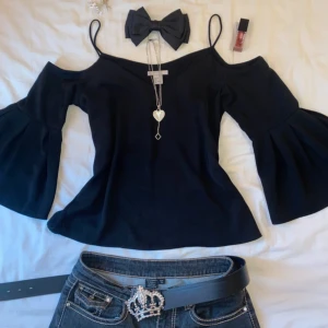 Svart offshoulder blus från H&M - Säljer en svart blus från H&M i storlek 34 med offshoulder och smala axelband. Blusen har vida, volangärmar och v-ringad hals. Materialet är mjukt och lätt, perfekt för att skapa en cool och trendig look.