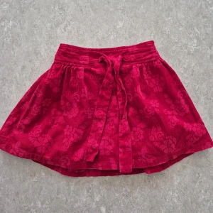 Kjol - Söt röd kortkjol från FIX med blommigt mönster och bred resår i midjan. Kjolen har ett knytband framtill och volangig tyll under för extra fluff. Materialet är mjuk manchester och kjolen har en loose passform som ger en skön och avslappnad look.