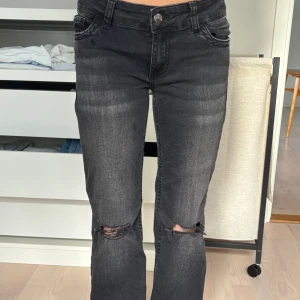 Svarta bootcut jeans med slitna knän - Säljer ett par svarta jeans från Nelly med bootcut passform och slitna detaljer vid knäna. Jeansen har klassiska fem fickor och snygga broderade bakfickor. Materialet är stretchigt jeans och färgen är svart med tvättade partier.