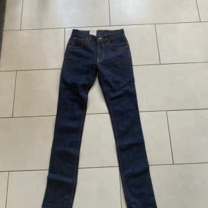 Nudie Jeans Tape Ted mörkblå jeans - Säljer ett par Nudie Jeans Tape Ted i mörkblå denim med kontrasterande orange sömmar och klassiska fem fickor. Jeansen har rak passform och snygga detaljer på bakfickorna. Perfekt för dig som gillar stilrena och tidlösa jeans.