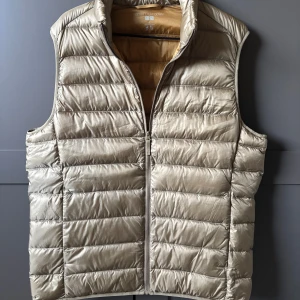 Beige dunväst från Uniqlo Ultra Light Down - Snygg beige dunväst från Uniqlo Ultra Light Down med quiltad design och dragkedja framtill. Nypris är 599 och denna är helt ny🙌Mitt pris:499(pris går att diskuteras!)