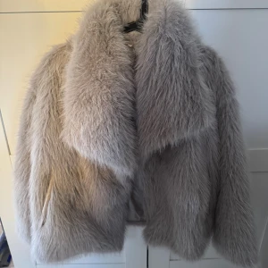 Beige fluffig pälsjacka - Säljer en supermjuk och fluffig pälsjacka i beige ton med bred krage och helfodrad insida. Jackan har långärmade ärmar och en oversized look helt ny och endast provad