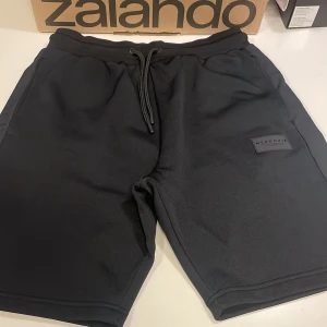 Svarta shorts från McKenzie med snörning - Svarta shorts från McKenzie i mjukt material med elastisk midja och snörning. Klassisk design med två sidofickor och diskret logga på vänster ben. Perfekta för chill eller träning, riktigt sköna och stilrena.