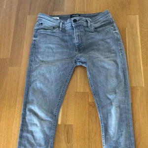 Grå skinny jeans Jack & Jones 30/30 - Snygga grå jeans från Jack & Jones i modellen Spray On/Tom. De har en skinny passform med smal siluett och klassisk femficksdesign. Jeansen är tillverkade i stretchigt denim för extra komfort och har en modern, ljusgrå tvätt.