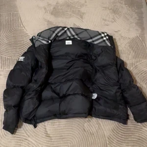 Svart pufferjacka från Burberry - Säljer en svart pufferjacka från Burberry med klassiskt rutigt foder i grå toner. Jackan har lång ärm, dragkedja och en patch med Burberry London England på armen. Perfekt för kalla dagar och har en riktigt schysst oversized vibe. Går att göra till väst också. Storlek M men passar även L.      PRISET GÅR ATT DISKUTERA!!