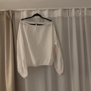 Vit volymblus från Nelly - Vit blus från Nelly med volym i ärmarna och rak, vid halsringning. Modellen är luftig med långa ärmar och resår i nederkant och ärmslut. Perfekt för dig som gillar en clean och stilren look.