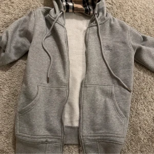 Grå hoodie från Burberry - Säljer en grå hoodie från Burberry som har ett rutigt mönster. Tröjan är som ny och har inte använts