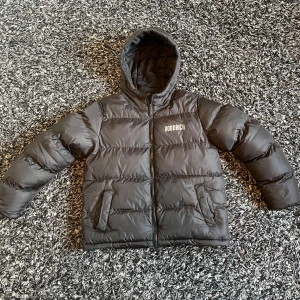 Svart pufferjacka från Hoodrich - Svart pufferjacka från Hoodrich med stor logga på ryggen och mindre tryck på bröstet. Jackan har huva, två fickor framtill och dragkedja med Hoodrich-detalj. Perfekt för kalla dagar och riktigt street i stilen. Säljer den eftersom den passar inte mig. Den passar för dem som har storlek xs. Skriv om du är intresserad, pris kan diskuteras.