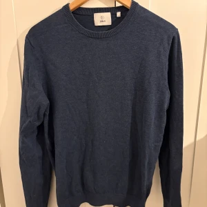 Mörkblå stickad tröja från Bläck - En stilren mörkblå stickad tröja från Bläck i storlek S. Tröjan har rund halsringning, ribbade muddar och är långärmad. Perfekt för lager-på-lager och enkel att matcha med jeans.