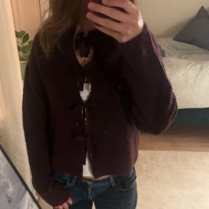 Vinröd stickad kofta med rosetter - Säljer en helt oanvänd vinröd stickad tröja med rosetter! Denna är i storlek 158/164 men passar mig med xs/s. Tröjan är superfin att ha både fram och bak! 