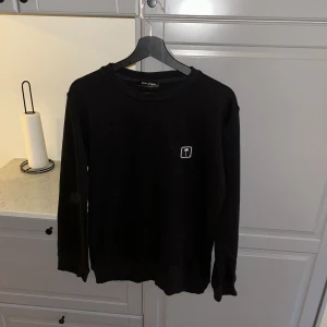 Svart sweatshirt från Palm Angels - Svart långärmad sweatshirt från Palm Angels med rund hals och liten vit logga på bröstet. Tröjan har en klassisk passform och är tillverkad i mjuk bomull, perfekt för en clean och stilren look.