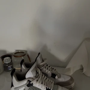  Jordan 4 military black - Nike Air Jordan 4 Retro sneakers i vit och svart med meshpaneler och klassisk Jumpman-logga på plösen och hälen. Skorna har snörning, platt sula och detaljer i syntet och skinn. Perfekt för dig som gillar streetwear och vill sticka ut med en ikonisk modell.