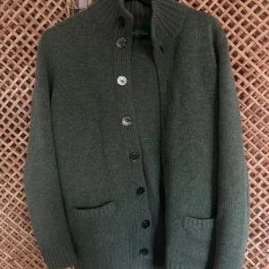 Grå kofta från Alan plain  - Snygg grå kofta från Alan plain med ribbad krage och knappar hela vägen framtill. Koftan har två praktiska fickor och är stickad i mjukt ullmaterial. Perfekt för dig som gillar klassisk stil med en chill vibe.