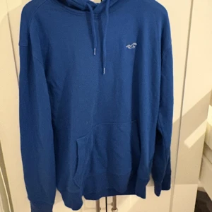 Blå hoodie från Hollister  - Säljer en blå hoodie från Hollister Must-Have Collection i storlek M. Tröjan har huva med snörning, en stor magficka och Hollisters logga broderad på bröstet. Perfekt för chill dagar.