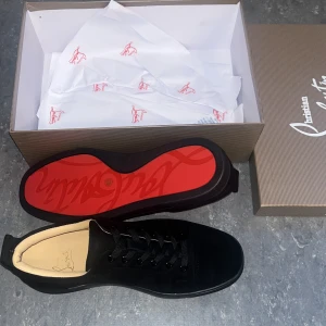 Christian Louboutin svarta sneakers - Säljer ett par svarta sneakers från Christian Louboutin i mocka med klassisk röd sula och svarta skosnören. Modellen heter Louis N Luck Flau Velours och har en stilren, rund tå och diskreta detaljer. Perfekta för dig som vill ha en lyxig och clean look. Storlek 43 säljer pga för stora för mig aldrig använt