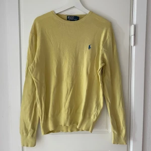Gul stickad tröja Polo Ralph Lauren - Snygg gul stickad tröja från Polo Ralph Lauren i slim fit-modell. Tröjan har rund hals och ett blått broderat logomärke på bröstet. Perfekt för dig som gillar klassisk stil med en färgklick. Passar dig som vill ha en enkel men stilren look. Liten i storleken.