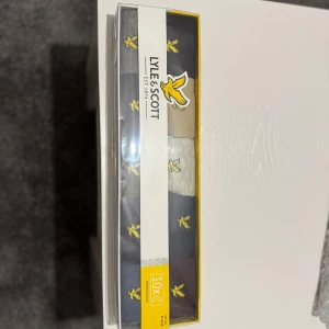 Lyle & Scott strumpor 10-pack - 10-pack strumpor från Lyle & Scott i olika färger som svart, grå, beige och blå. Alla strumpor har broderade gula fåglar som detalj. Klassisk och stilren design, perfekt för dig som gillar att hålla det enkelt men ändå vill ha något extra. Äkta såklart 