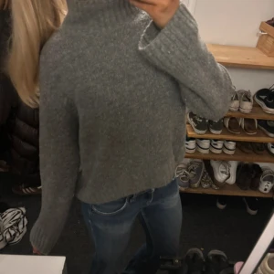 Grå stickad polotröja - Mysig grå stickad polotröja med hög krage och långa ärmar. Tröjan har en loose passform och är perfekt för kyliga dagar. Materialet är mjukt och ger en chill vibe, enkel att matcha med jeans eller andra favoritplagg.