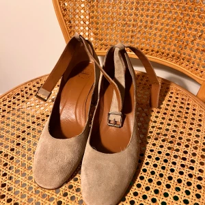 Beige mockapumps från ATP Atelier - Snygga pumps från ATP Atelier i beige mocka med rund tå och låg klack. Skorna har en elegant rem med spänne över vristen och är tillverkade i Italien. Perfekta för dig som gillar stilrena och klassiska skor med en modern twist.