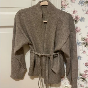 Beige stickad kofta med knytband - Mysig beige stickad kofta med långa ärmar och ribbade muddar. Ljusbrun kofta, använd en gång så i nytt skick! Köptes på Plick, har ingen lapp tyvärr.