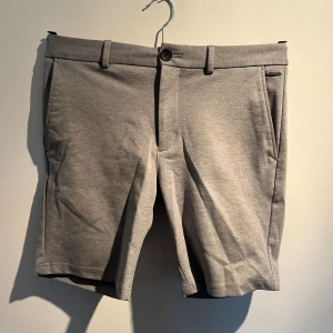 Grå shorts med fickor - Snygga grå shorts med klassisk design. De har bälteshällor, framfickor och två bakfickor med knapp. Materialet är mjukt och känns som bomull eller polyester, perfekt för chill dagar. Stängs med knapp och dragkedja framtill.