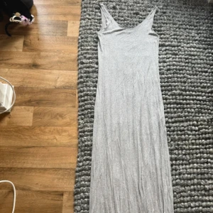 Grå långklänning från Vila - En enkel och stilren grå långklänning från Vila med ärmlös design och rundad halsringning. Klänningen är gjord i mjuk bomull och har en rak passform som faller snyggt längs kroppen. Perfekt för dig som gillar minimalistisk stil.