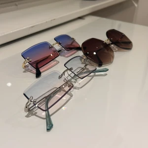 3 trendiga glasögon från SHEIN - Säljer tre par glasögon från SHEIN: ett par rektangulära med transparenta blåtonade glas och silverdetaljer, ett par rektangulära med färgskiftande blå-rosa glas och gulddetaljer, samt ett par stora åttakantiga solglasögon med bruna glas och gulddetaljer. Alla med svarta fodral.