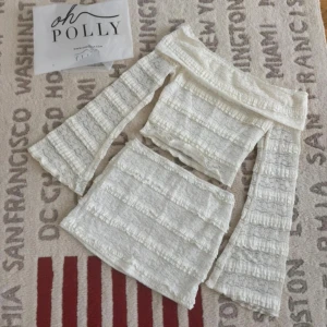 Vit offshoulder spetsblus Oh Polly - Supersöt vit offshoulder blus från Oh Polly med långa utsvängda ärmar. Blusen är croppad och har volangdetaljer och spets över hela tyget för en romantisk vibe. Perfekt att matcha med kjol eller jeans för en trendig look.