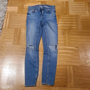 Blå skinny jeans från G Perkt Jeans - Snygga blå jeans i modellen Kristen från G Perkt Jeans. Skinny fit med slitna detaljer och hål vid knäna för en cool look. Klassisk femficksdesign, dragkedja och knapp framtill. Perfekta för dig som gillar streetstyle.