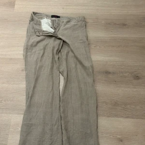 Beige linnebyxor från Mari Philippe - Snygga beige linnebyxor från Mari Philippe i storlek 36. Byxorna har en rak och lite loose passform med klassisk knappstängning och bälteshällor. Perfekta för en chill och stilren look under varmare dagar.