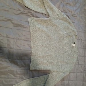 Grå stickad v-ringad tröja Divided - Mysig grå stickad tröja från Divided by H&M i storlek XXS. Tröjan har v-ringning, lång ärm och en klassisk, enkel design som är lätt att matcha. Perfekt för lager-på-lager under kyliga dagar.