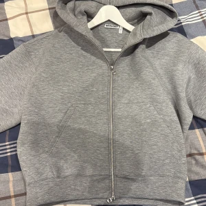 Grå hoodie med dragkedja från Weekday - Säljer en stilren grå hoodie från Weekday i storlek L. Tröjan har huva, hel dragkedja framtill och två fickor. Materialet är mjukt och känns skönt mot huden, perfekt för chill dagar. Klassisk passform och långärmad design.