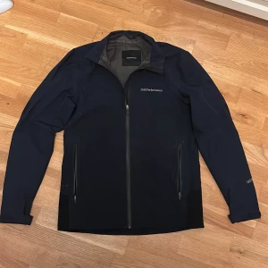 Mörkblå vindjacka Peak Performance S - Peak Performance vindjacka i mörkblått med stilren design och diskret logga på bröstet. Jackan har hel dragkedja framtill, två sidofickor med dragkedja och långärmade ärmar. Materialet är slitstark polyester och jackan är perfekt för blåsiga dagar. Nypris runt 1300kr