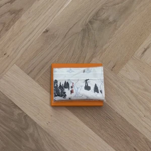 vit plånbok med vintermotiv - Exklusiv korthållare i vitt skinn med vinterinspirerat tryck. Motivet visar skidåkare, liftar och snötäckta granar. 