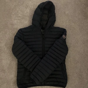 Svart pufferjacka från Colmar - Mörkblå pufferjacka från Colmar med huva och dragkedja framtill. Jackan har ett quiltat mönster och Colmar-logga på ärmen. Perfekt för kyliga dagar och har en clean, sportig vibe. Passar dig som gillar stilren och funktionell design.