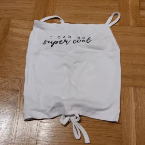 Vit linnetopp med snörning och text - Säljer en vit linnetopp från Ladieswear med smala axelband och snörning baktill. Toppen har trycket 'I can be super cool' framtill i svart. Materialet är mjuk bomull med lite stretch för skön passform. Perfekt för dig som gillar enkel och snygg stil.