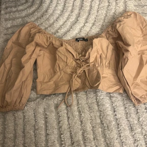 Beige omlott blus från Bik Bok - Säljer en beige blus från Bik Bok i storlek S. Modellen är croppad med omlott och snörning framtill, har offshoulder och långa puffärmar. Materialet är mjuk bomull med smockad rygg och elastiska detaljer vid ärmslut. Perfekt för dig som gillar trendiga och feminina toppar.