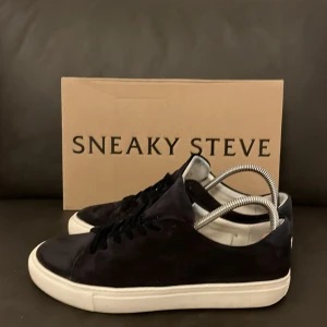 Svarta sneakers från Sneaky Steve - Stilrena svarta sneakers från Sneaky Steve med vit platt sula och svarta snören. Skorna är låga och har en klassisk rund tå. Ovandelen är i mocka och insidan är fodrad i vitt. Perfekta för dig som gillar minimalistisk och clean stil. Använt få tal gånger, har haft dom i cirka 2 veckor.